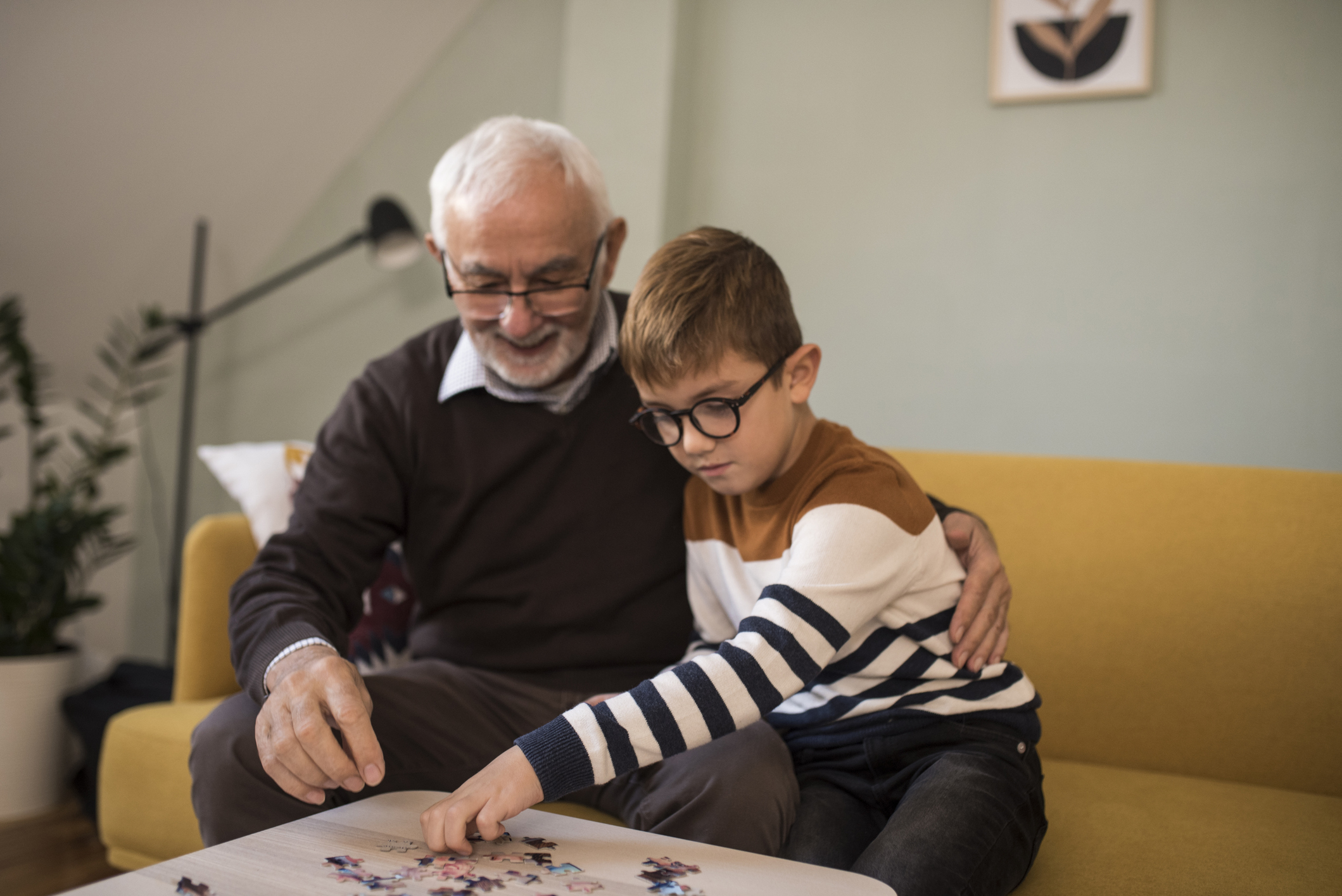 Bestefar byggjer Lego saman med barnebarnet sitt på eit lyst stuebord.