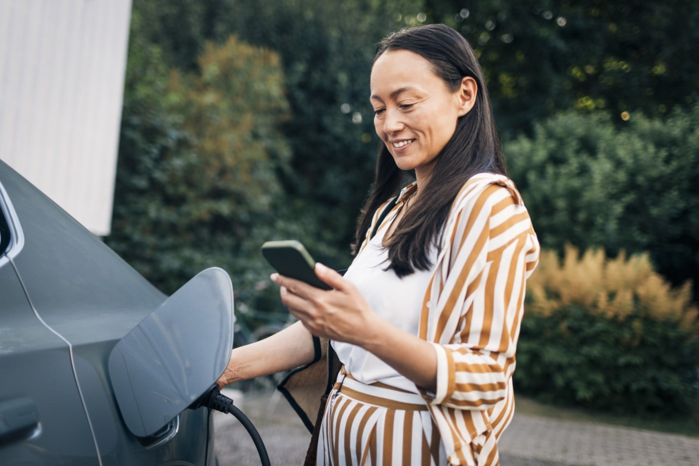 vinne som ladar elbil og sjekkar mobilbank på mobilen – eit bilete på oversikt og ein moderne kvardag
