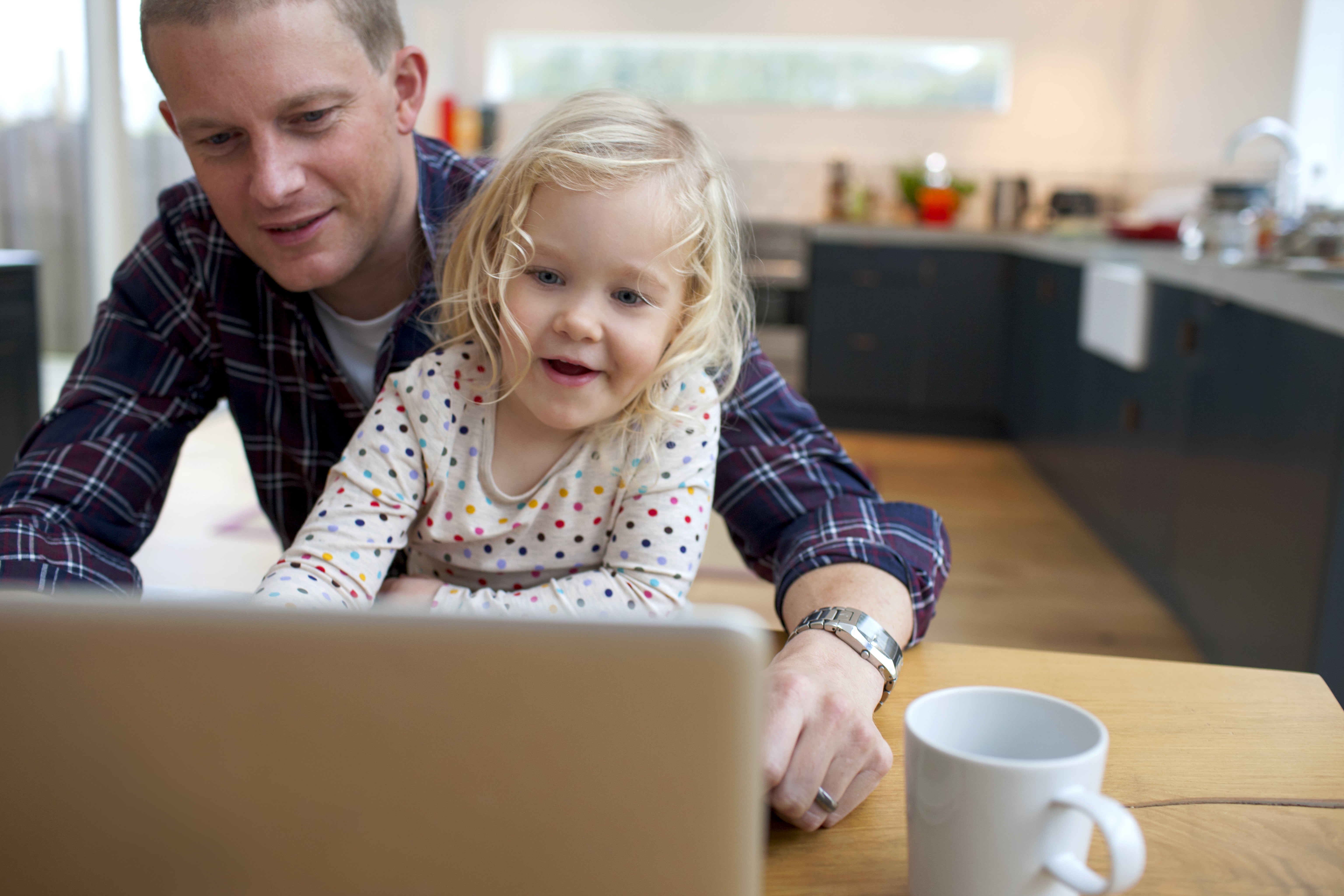 Person med rutete skjorte og klokke på handledet, sit ved bord med kaffikopp og berbar PC.