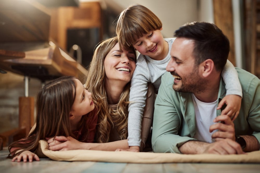 Ein familie som ligg på golvet heime, alle smiler og ler saman, og viser eit augeblink av rein glede.