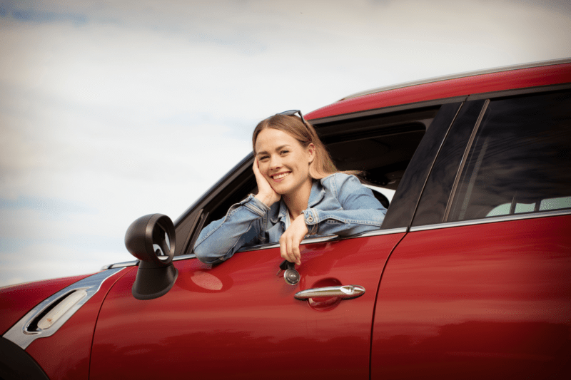En dame lener seg ut av bilvinduet med en bilnøkkel i hånden