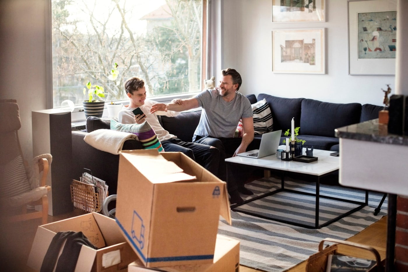 Ein mann og ein ung gut sit i sofaen med pappøskjer på stovegolvet