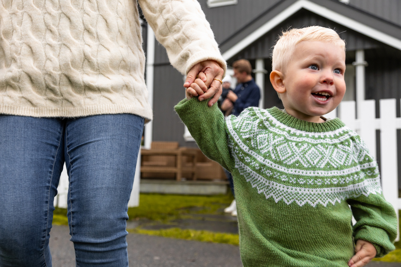 Blid gut med grøn genser som held mammaen sin i handa