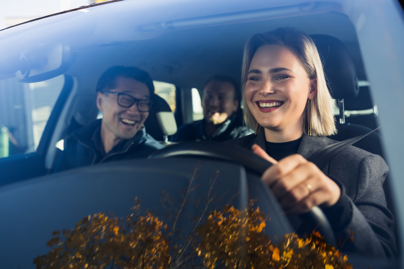 Blid dame som køyrer bil med to mannlege passasjerar