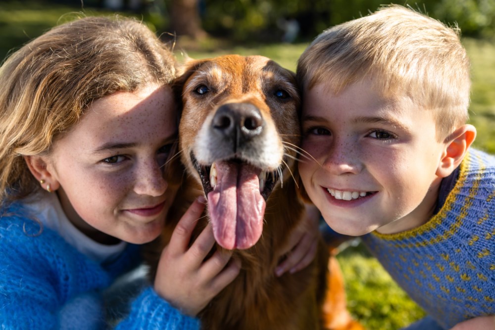 Jente og gut kosar med hunden mellom seg