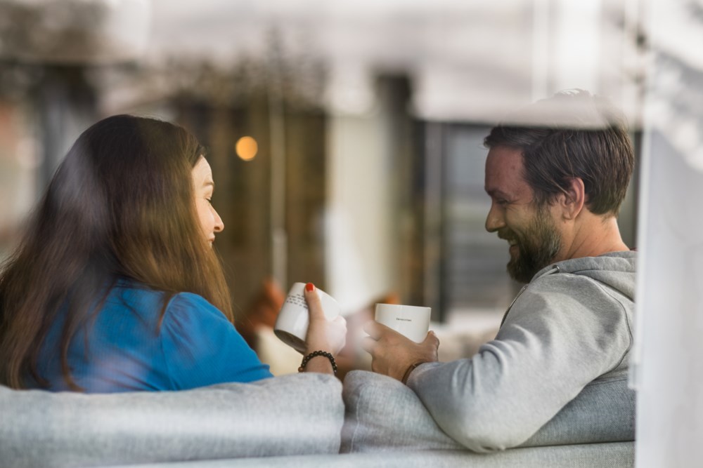 Ser inn mot kvinne og mann som sit i sofaen med ein kaffikopp kvar